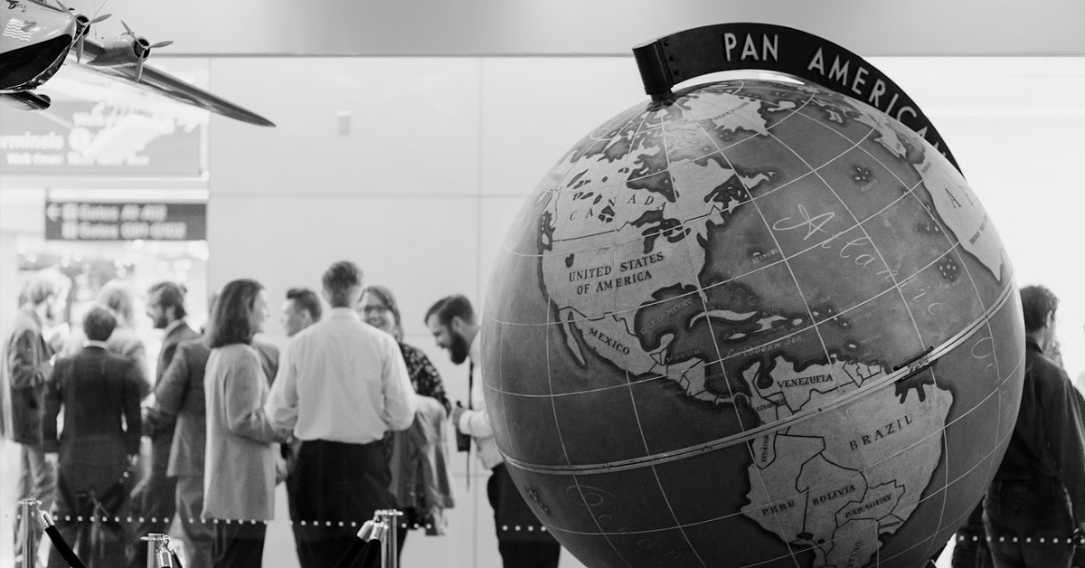 A black and white photo of people mingling during a wedding reception, beside a large globe with Pan Am branding.