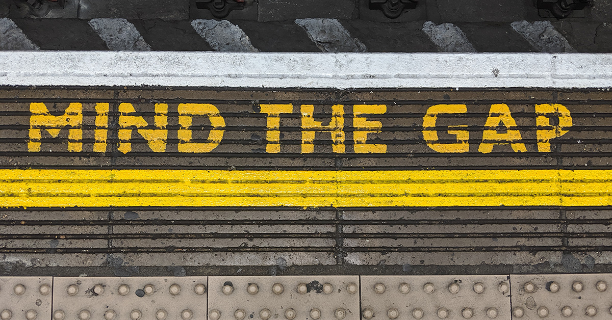 A photo of the words "mind the gap" written in yellow paint on the ground in an underground train station in London.